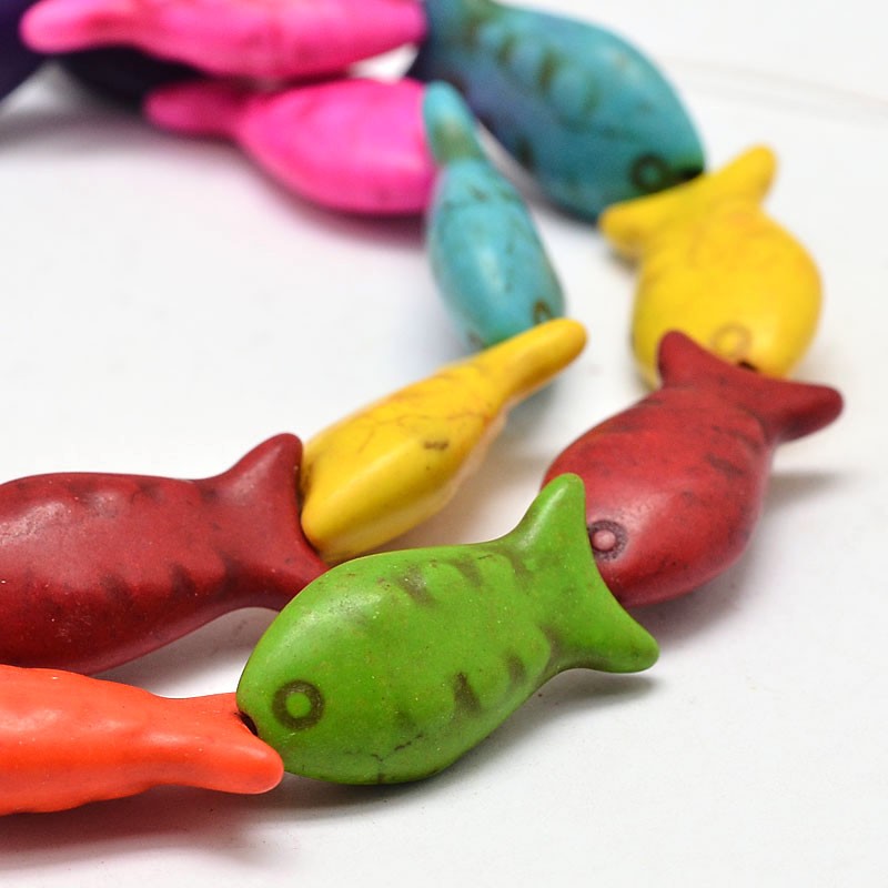 zoomed in sections of multicolor dyed magnesite fish bead strand over white background. 