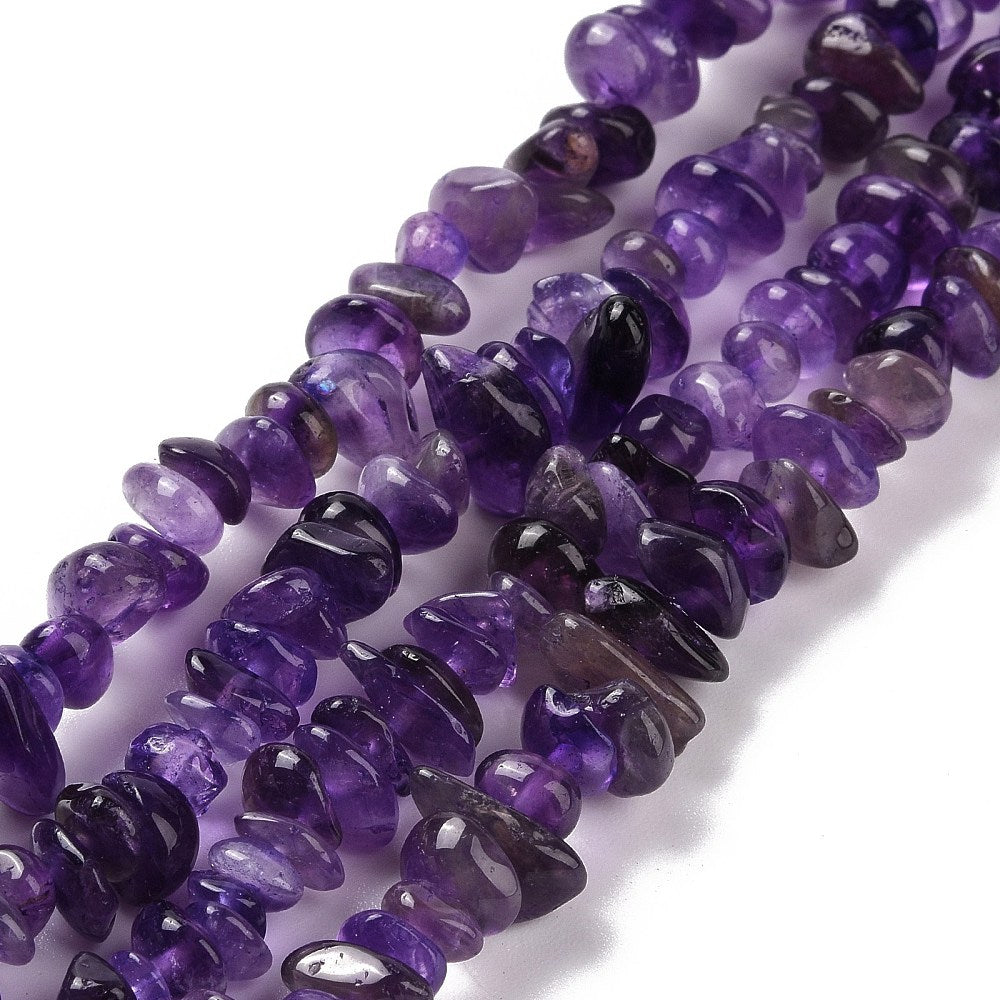 zoomed in sections of dark purple tumbled amethyst chip bead strand over white surface. 