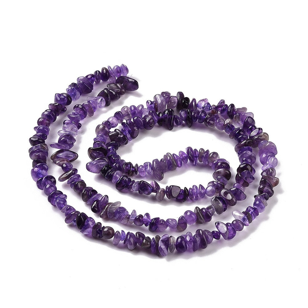 dark purple tumbled amethyst chip bead strand in swirl design over white surface. 