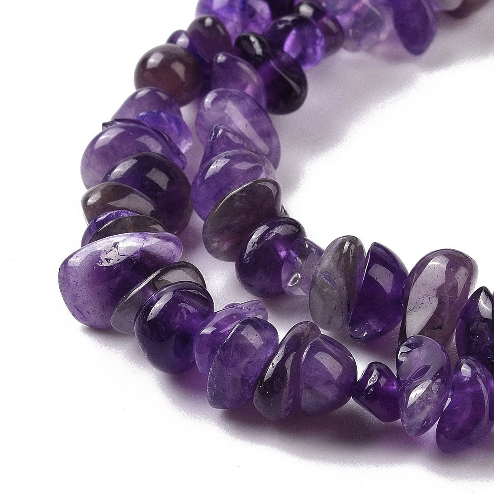 zoomed in sections of dark purple tumbled amethyst chip bead strand over white surface. 