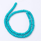 dyed turquoise magnesite rondelle bead strand in spiral design over white background. 