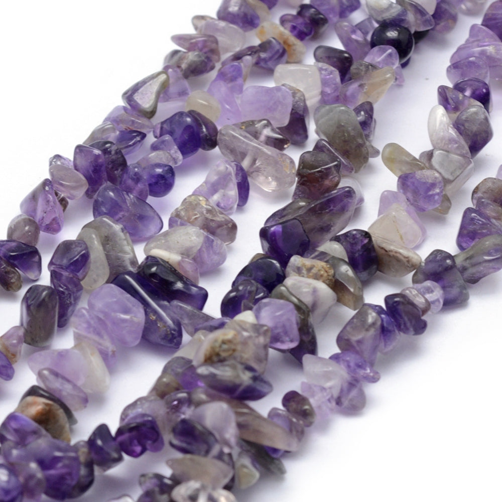 zoomed in sections of light purple tumbled amethyst chip bead strand over white surface. 