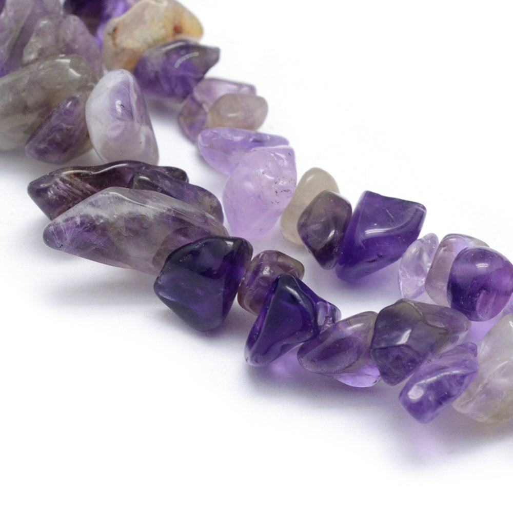 zoomed in sections of light purple tumbled amethyst chip bead strand over white surface. 