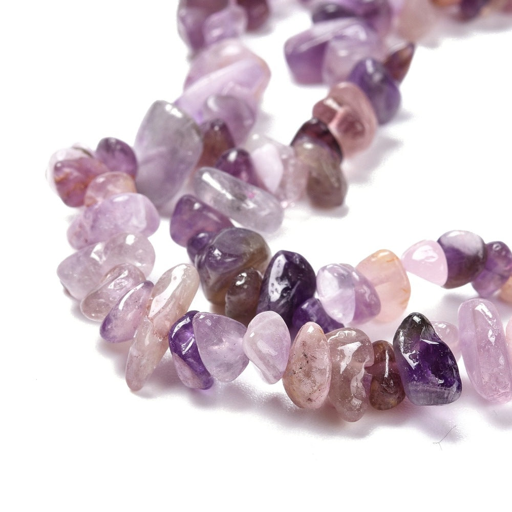zoomed in sections of light purple tumbled amethyst chip bead strand over white surface. 