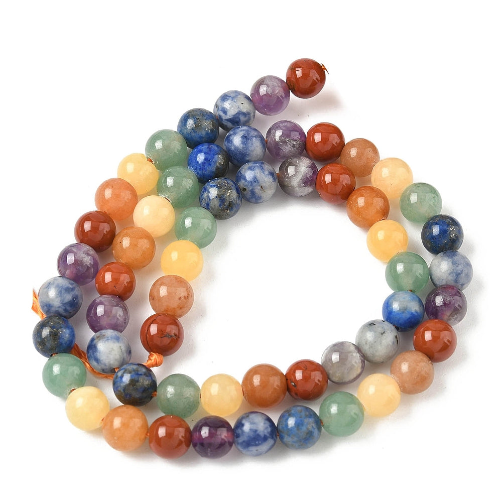 natural mixed gemstone chakra bead strand in swirl display over white surface. 
