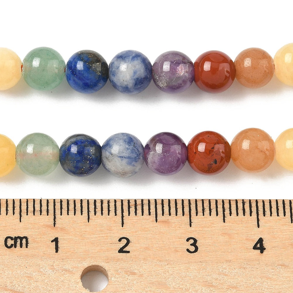zoomed in sections of natural mixed gemstone chakra bead strand displayed over wooden ruler on white surface. 
