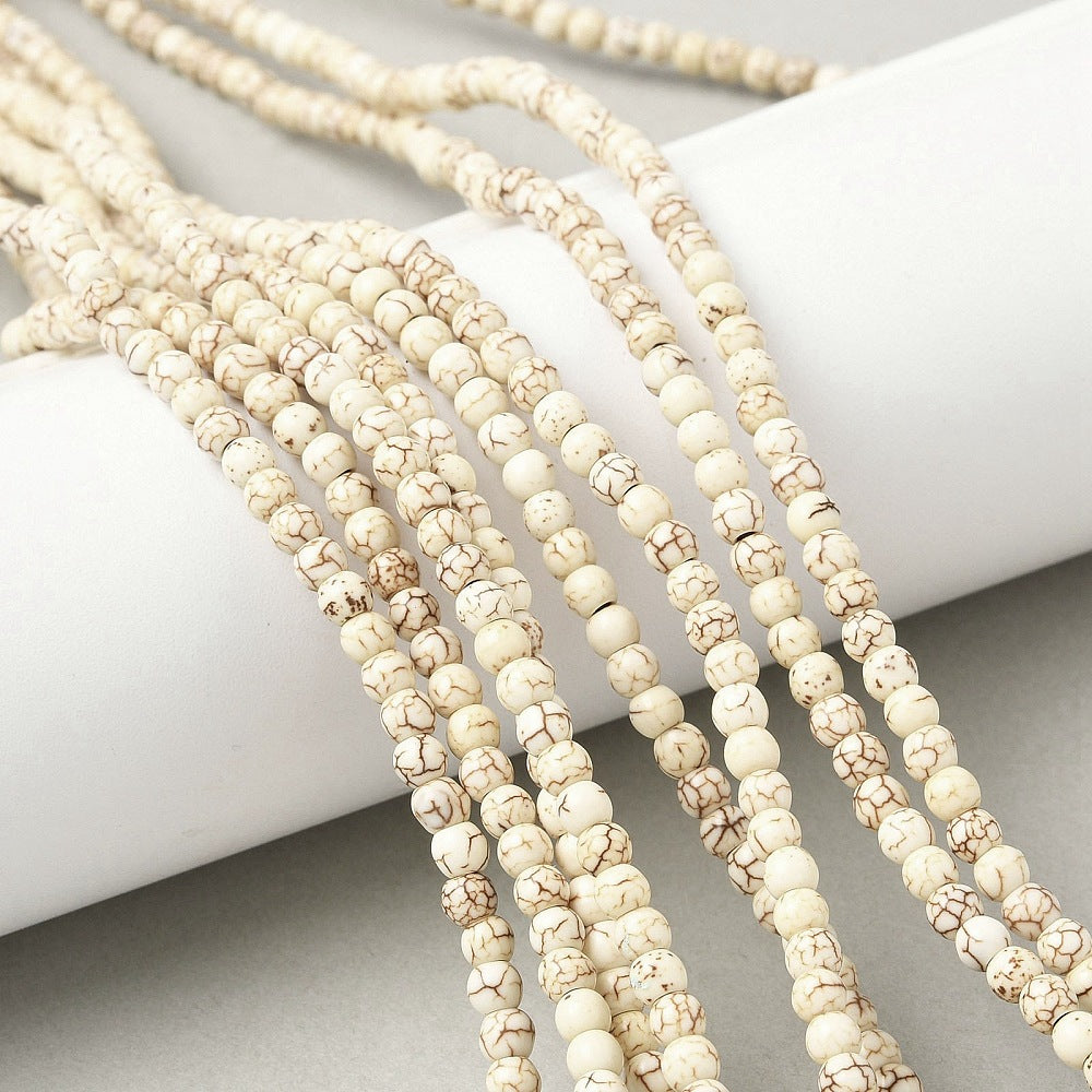 multiple off-white round magnesite bead strands draped over white cylinder form onto light grey surface. 