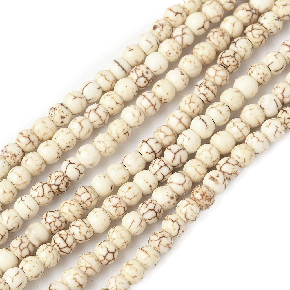 zoomed in sections of off-white round magnesite bead strand over white surface. 