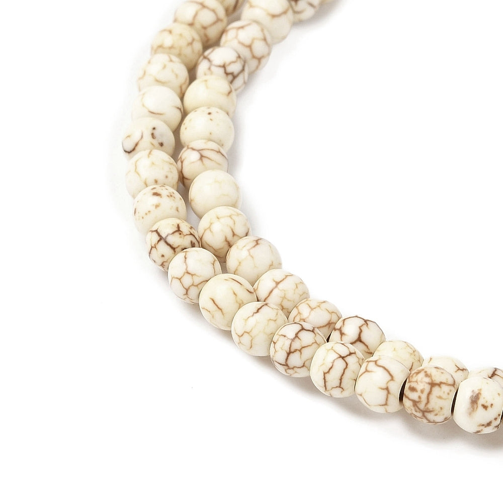 zoomed in sections of off-white round magnesite bead strand over white surface. 