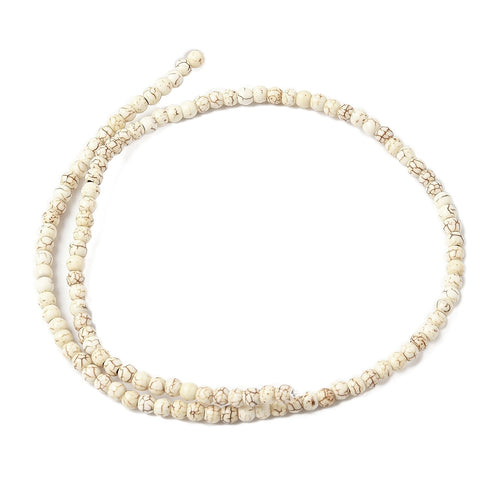 off-white round magnesite bead strand in swirl display over white surface. 