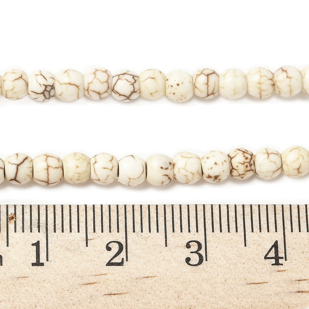 zoomed in sections of off-white round magnesite bead strand displayed over wooden ruler on white surface. 