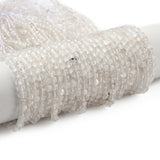 many clear quartz faceted cube bead strands wrapped around white cylinder form over white background. 