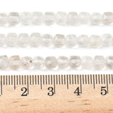 three zoomed in sections of clear quartz faceted cube bead strands displayed over wooden ruler with a white background. 