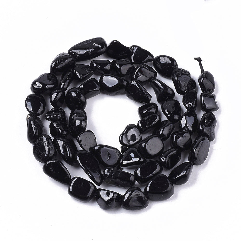 strand of tumbled black tourmaline nugget beads in a swirl design over white background. 