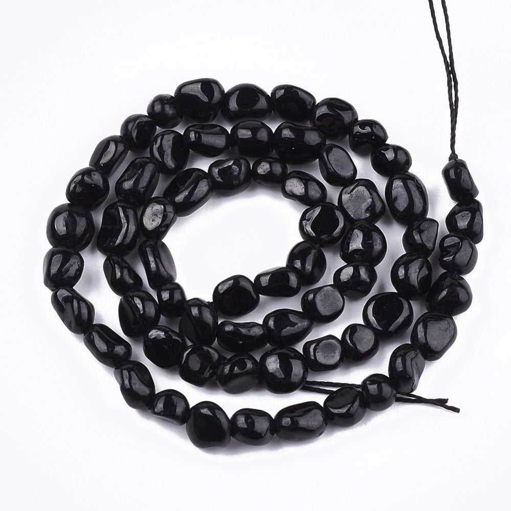 strand of tumbled black tourmaline nugget beads in a swirl design over white background. 