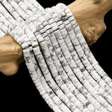 ten natural Howlite Heishi bead strands  draped over a piece of driftwood onto a black surface. 