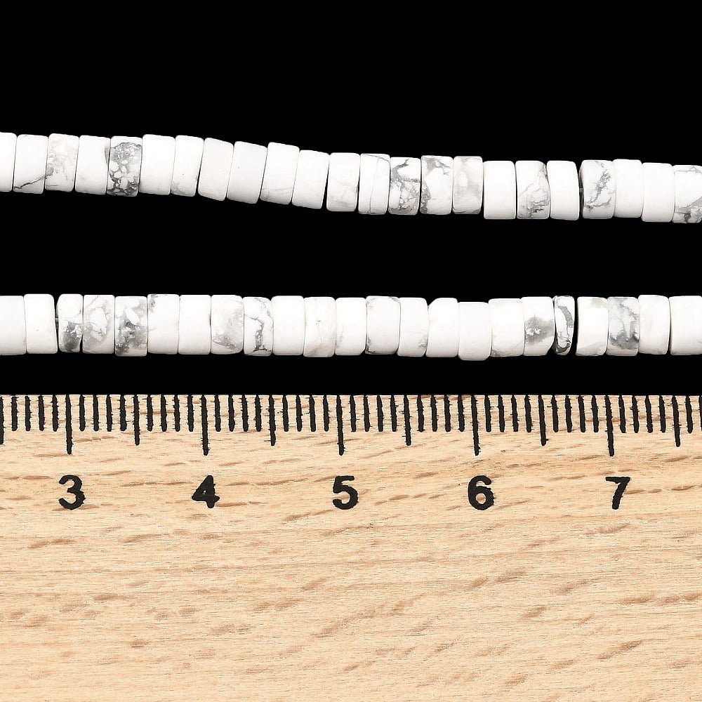 two zoomed in sections of natural Howlite Heishi bead strands displayed above a wooden ruler over a black background. 