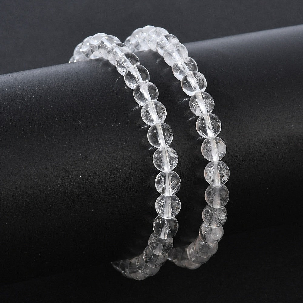 two round clear quartz crystal bead stretch bracelets around black cylinder form over black background. 