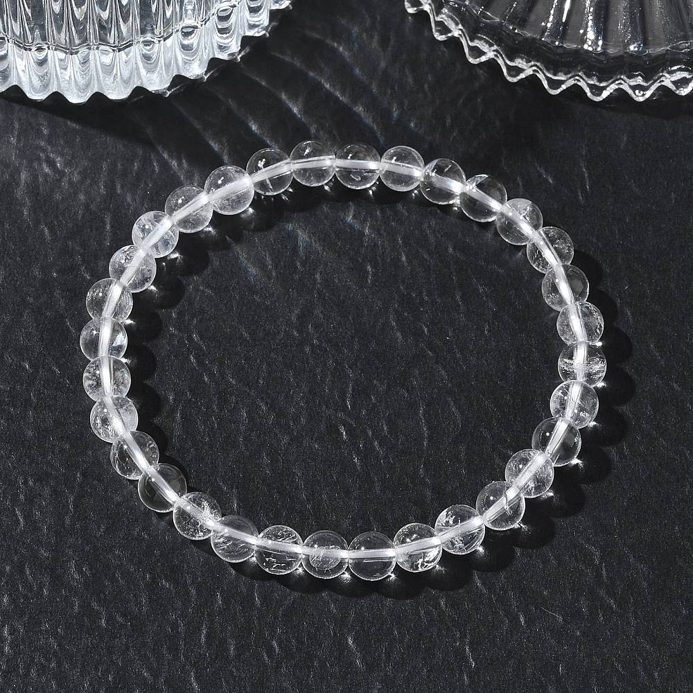 round clear quartz crystal bead stretch bracelet displayed on textured black surface with crystal glasses peeking in from the top. 