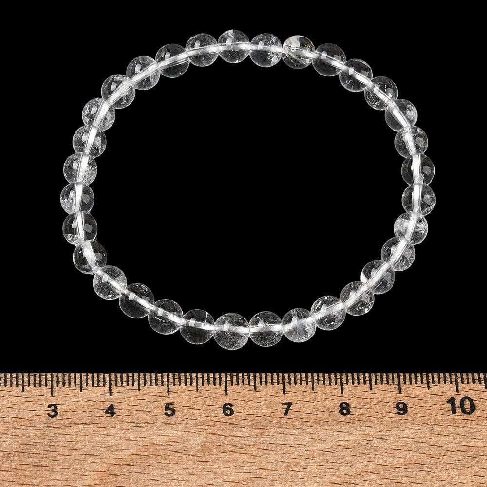 round clear quartz crystal bead stretch bracelets above wooden ruler over black background. 