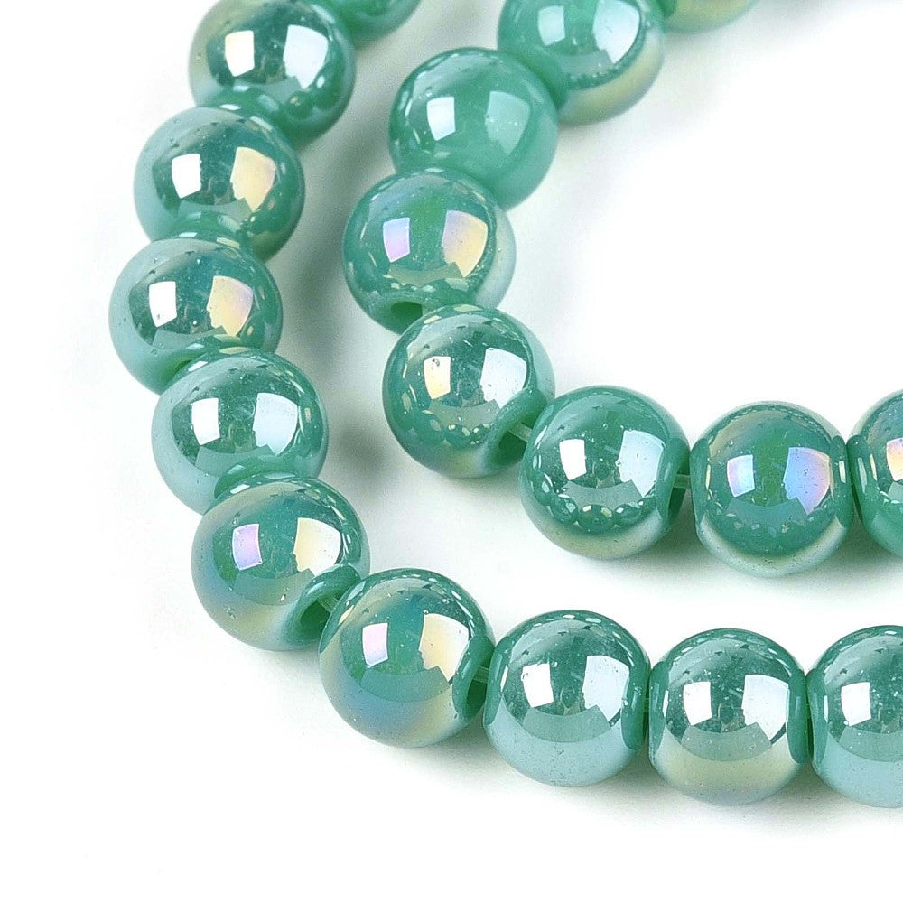 zoomed in sections of iridescent  turquoise green glass bead strand over white surface.  