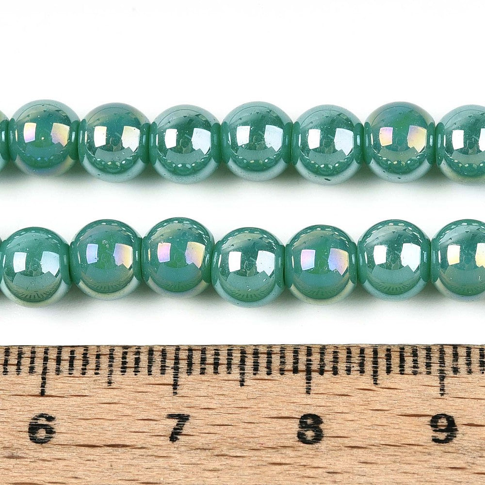iridescent turquoise green glass bead strand displayed above wooden ruler with white background. 