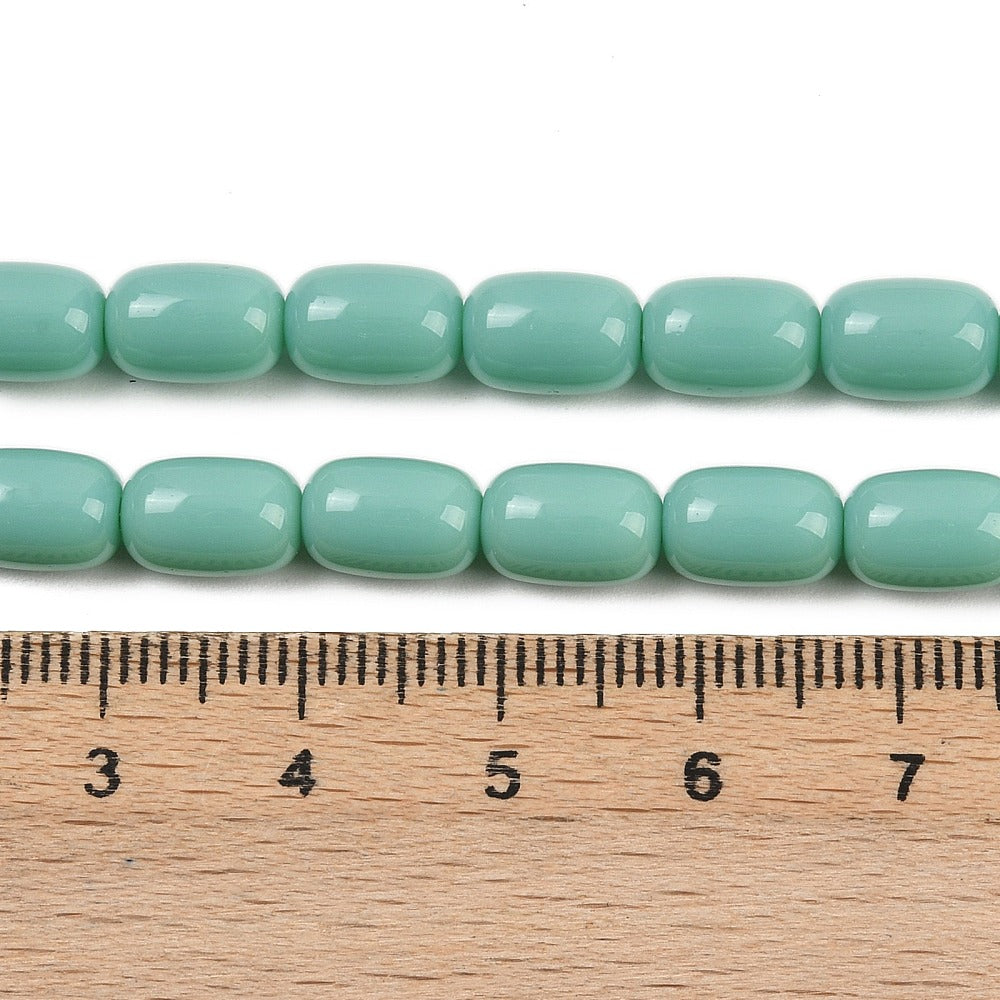 zoomed in sections of turquoise green barrel bead strands above wooden ruler over white surface.