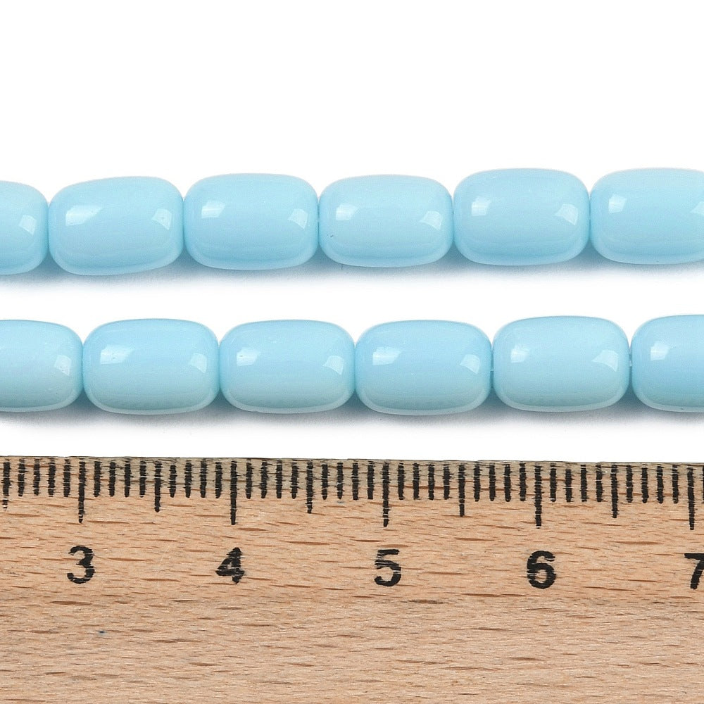 zoomed in sections of sky blue barrel bead strands above wooden ruler over white surface.