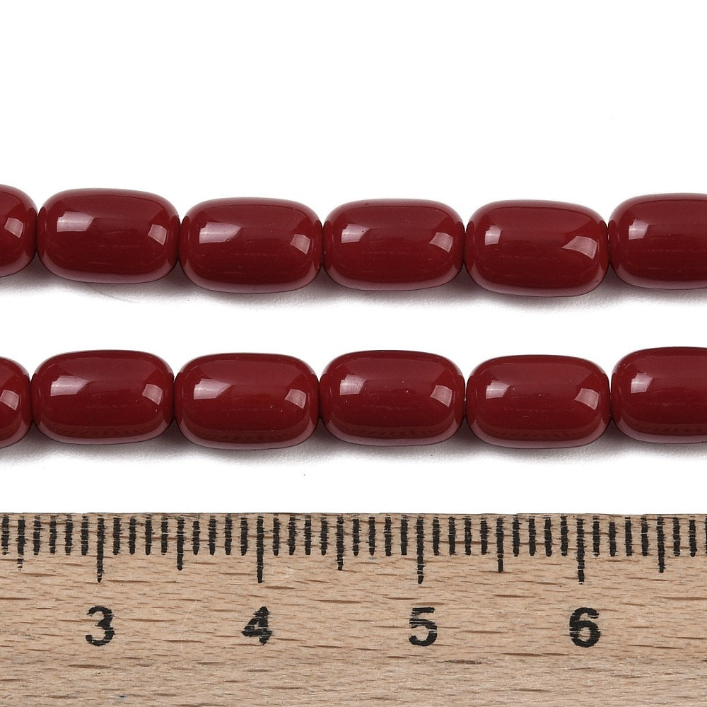 zoomed in sections of red barrel bead strands above wooden ruler over white surface.