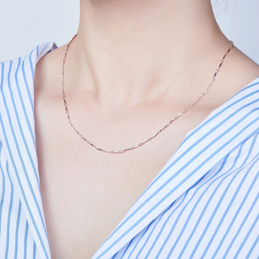 silver pinched bar link chain necklace displayed on neck with blue and white striped shirt with white background. 