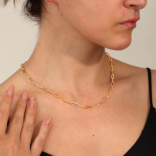golden flat paperclip chain necklace displayed on a women's neck against white background. 