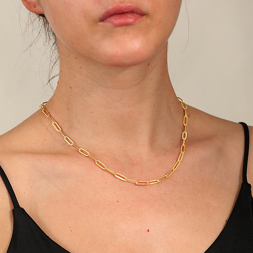 golden flat paperclip chain necklace displayed on a women's neck against white background. 