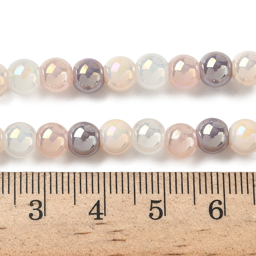 zoomed in sections of iridescent  opaque pink and purple glass bead strand above wooden ruler over white surface. 