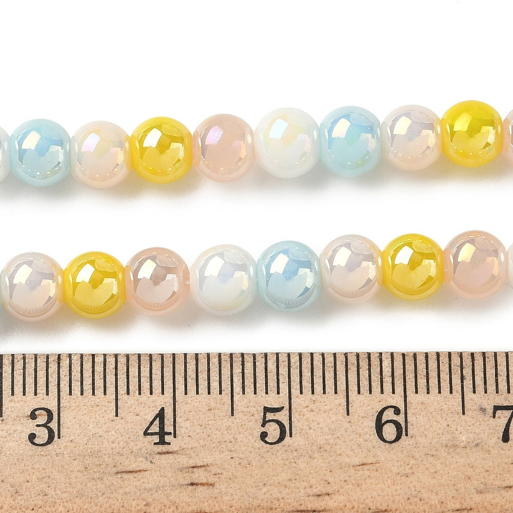 zoomed in sections of iridescent opaque blue and yellow glass bead strand above wooden ruler over white surface. 