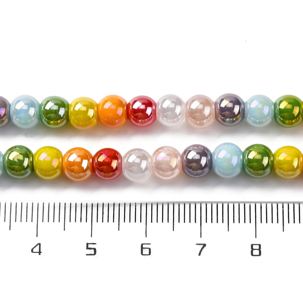 zoomed in sections of iridescent opaque rainbow glass bead strand above clear ruler over white surface. 
