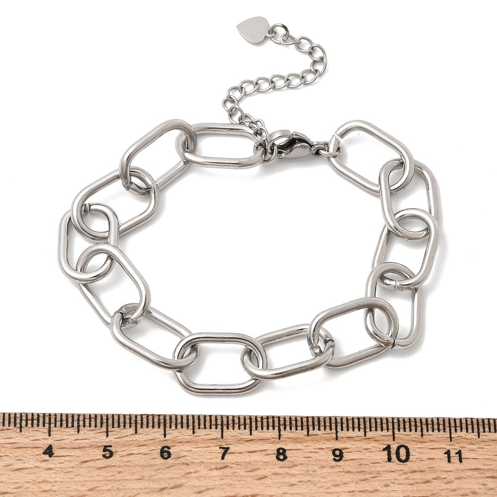 silver tone large oval cable link chain bracelets with lobster claw clasp and extender chain with heart charm above wooden ruler over white background. 