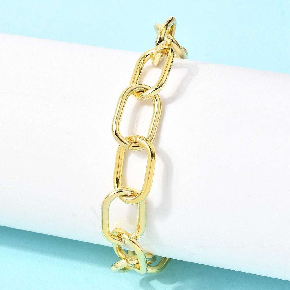 golden large oval cable link chain bracelet wrapped around white cylinder form over light blue surface. 