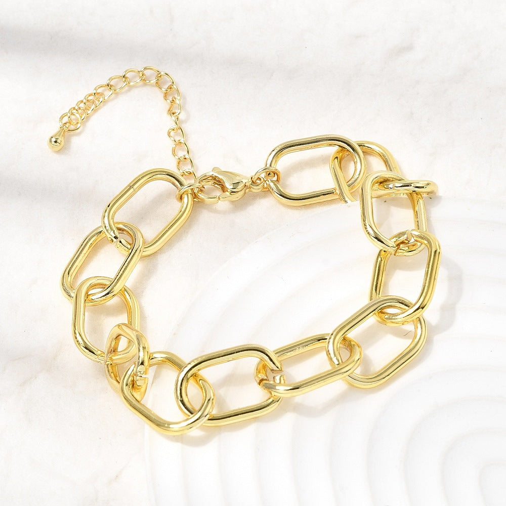 golden large oval cable link chain bracelets with lobster claw clasp and extender chain draped over off-white tray onto off-white surface.