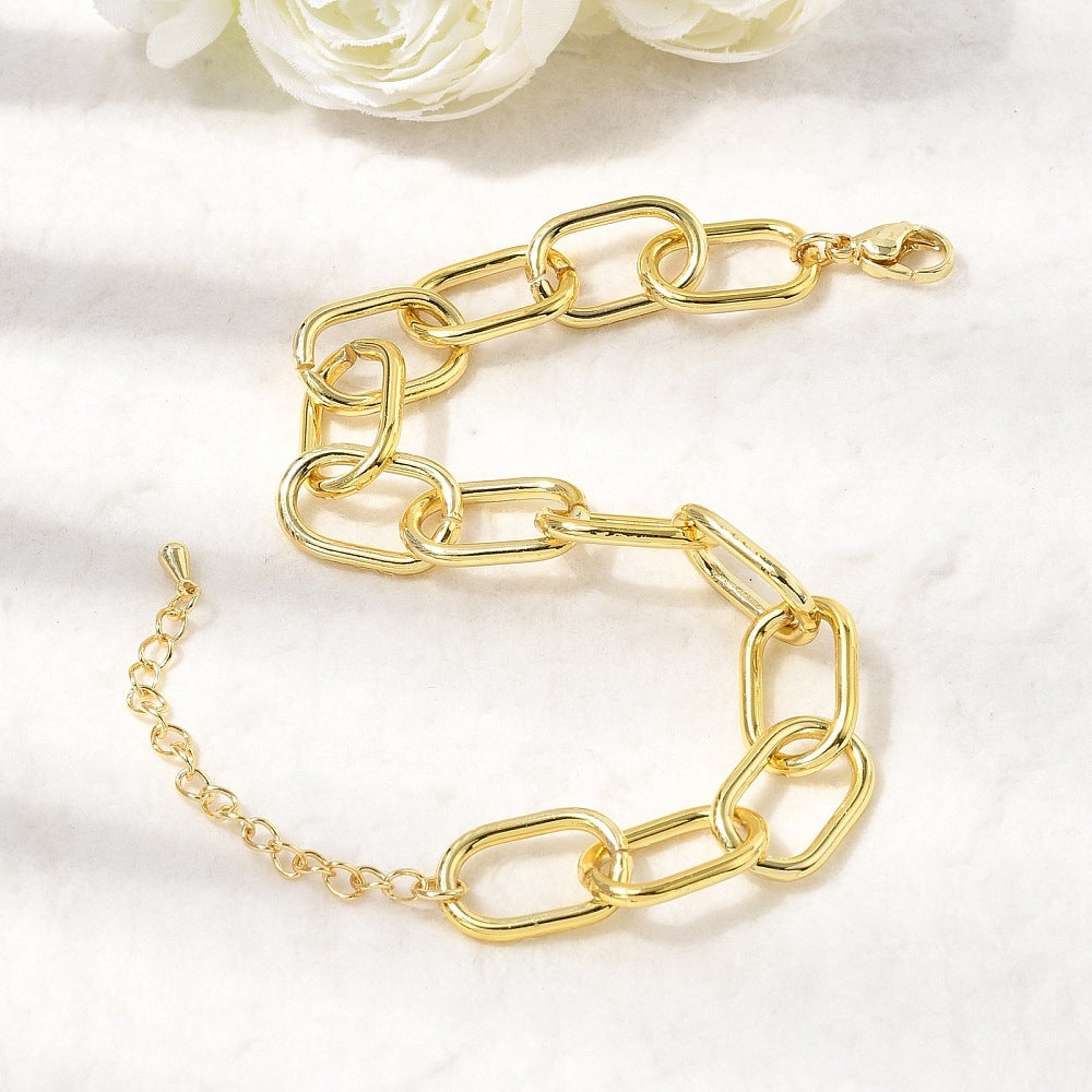 golden large oval cable link chain bracelets with lobster claw clasp and extender chain displayed on an off-white surface with white roses peeking in from the top. 