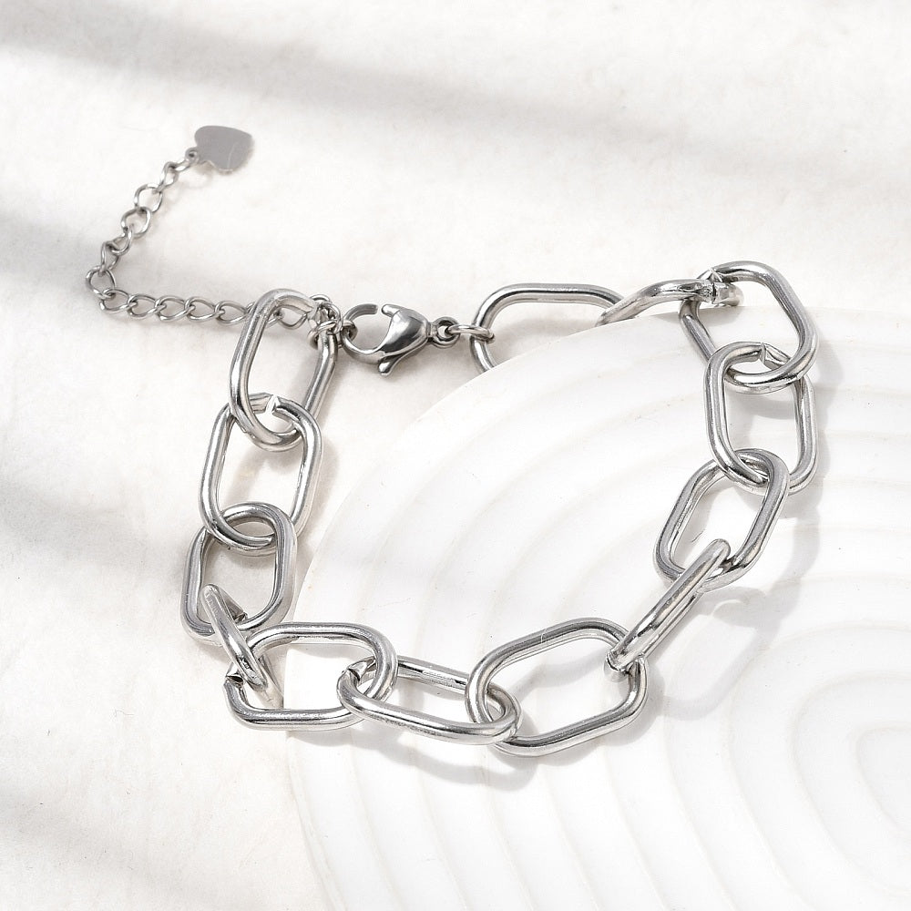 silver tone large oval cable link chain bracelets with lobster claw clasp and extender chain with heart charm draped over off-white tray onto off-white surface.