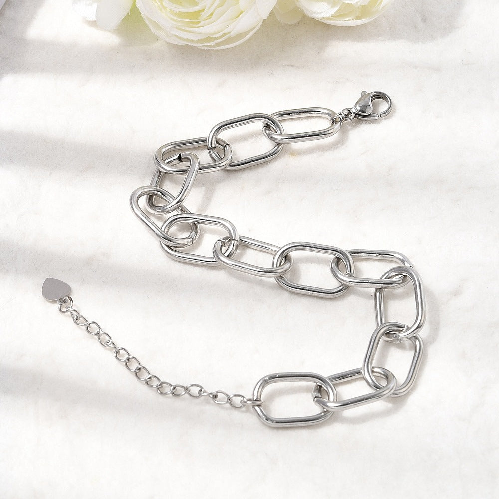 silver tone large oval cable link chain bracelets with lobster claw clasp and extender chain with heart charm displayed on an off-white surface with white roses peeking in from the top. 