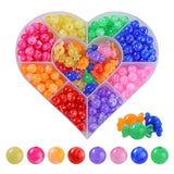 heart shaped plastic bead box divided into nine sections containing large hole round beads in green, blue, pink, purple, red, orange, magenta and yellow and the center section filled with multi-colored candy shaped beads. there are also examples of the loose beads below the box over a white background. 