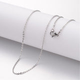 silver tone flat cable chain necklace with lobster claw clasp draped over white cylinder form over white background. 