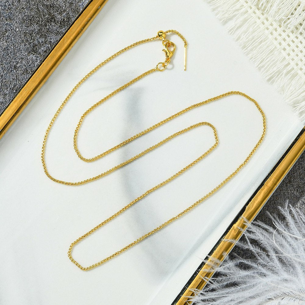 golden box chain adjustable slider necklace with lobster claw clasp, slider bead and stopper on gold rimmed tray on grey surface with white tassels and feathers peeking in the corners. 