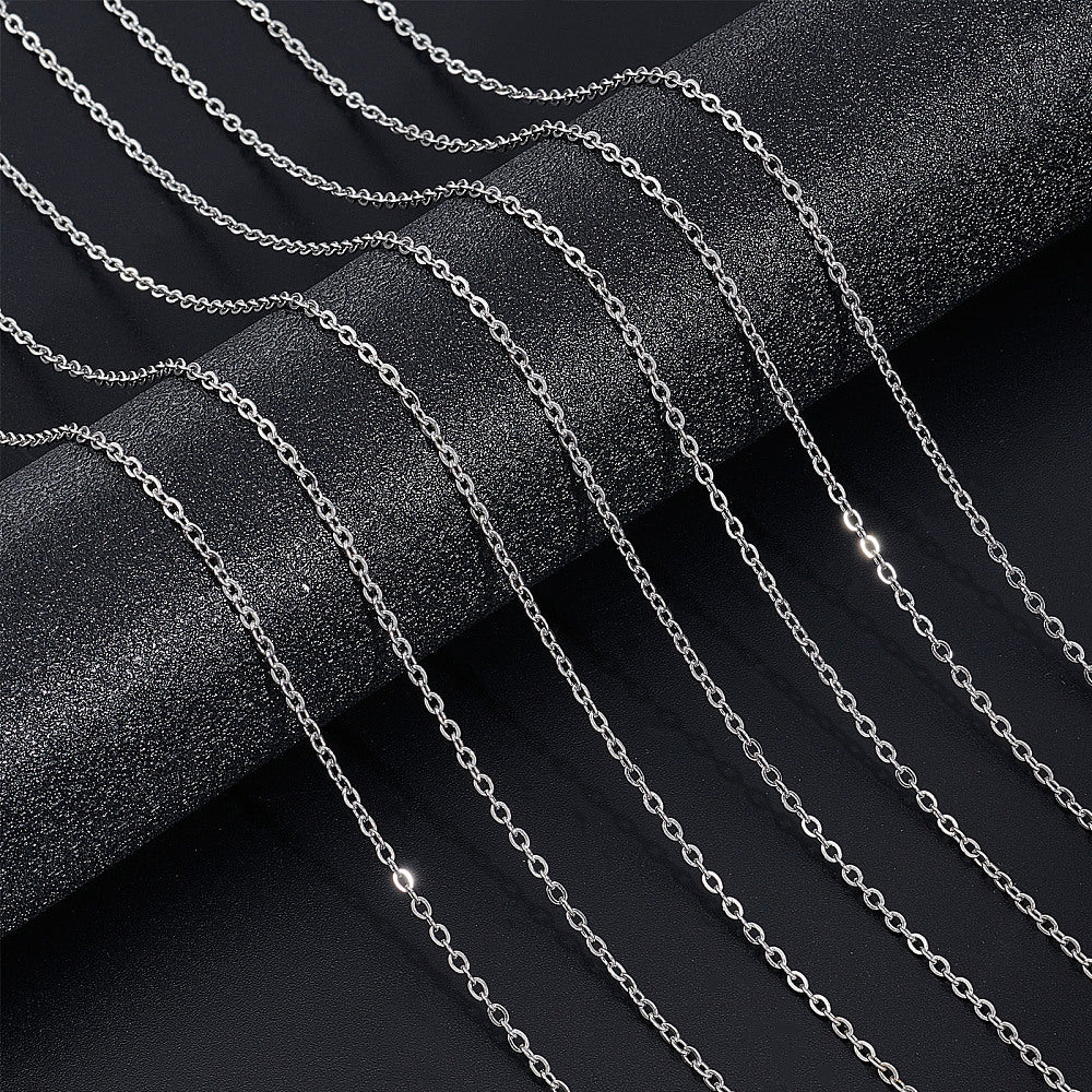 seven silver tone small cable chain necklaces draped over black textured cylinder onto black surface.