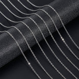 seven silver tone small cable chain necklaces draped over black textured cylinder onto black surface.