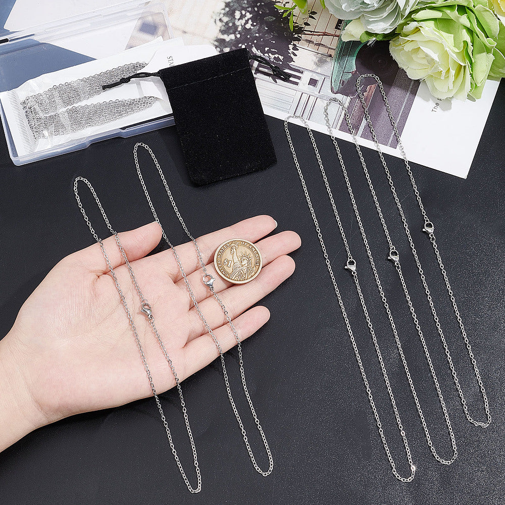 two silver tone small cable chain necklaces with lobster claw clasps displayed over a hand with a dollar coin in it and three more necklaces next to the hand on a black textured surface.