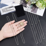 two silver tone small cable chain necklaces with lobster claw clasps displayed over a hand with a dollar coin in it and three more necklaces next to the hand on a black textured surface.