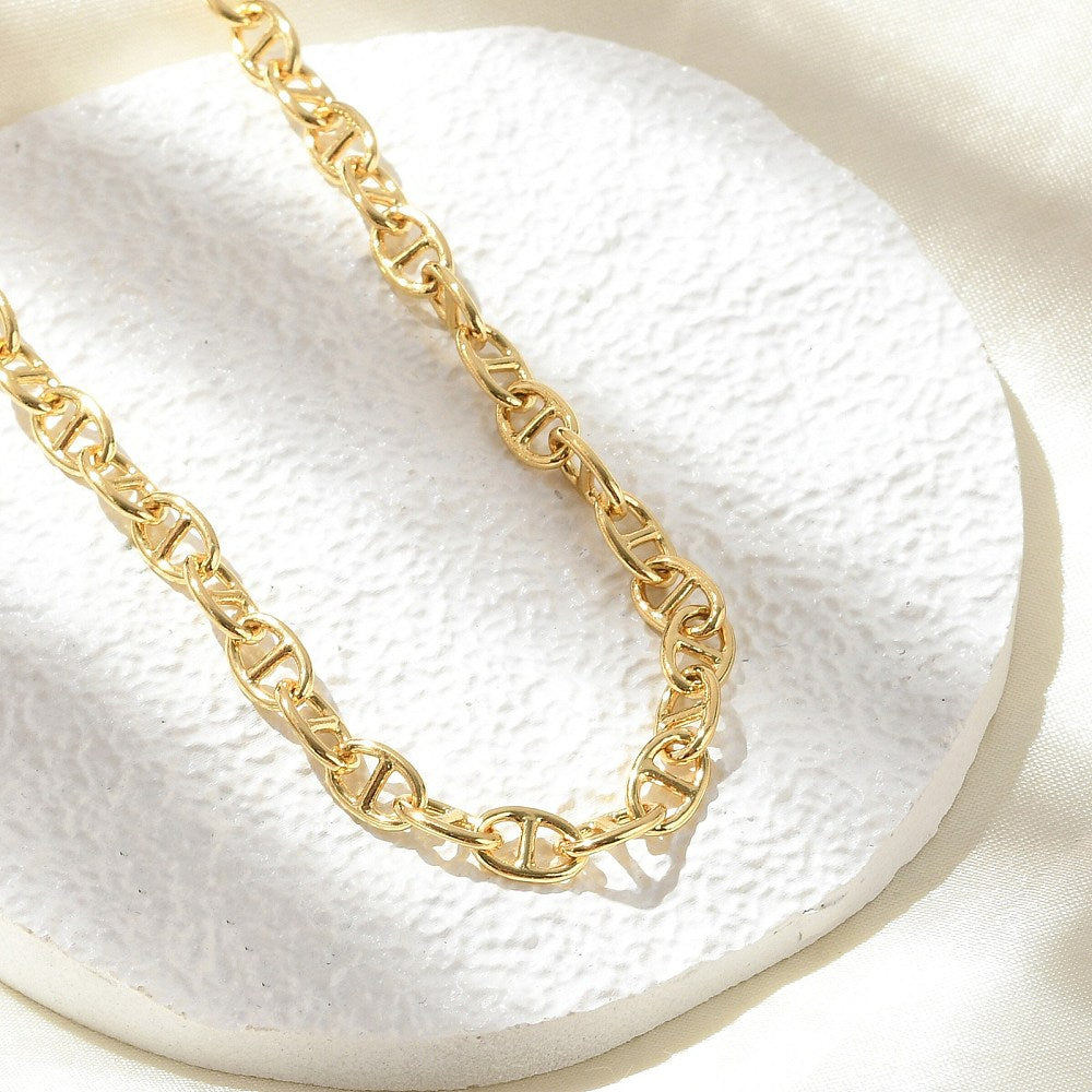 zoomed in section of golden oval mariner link chain on white textured coaster on an off-white cloth surface.