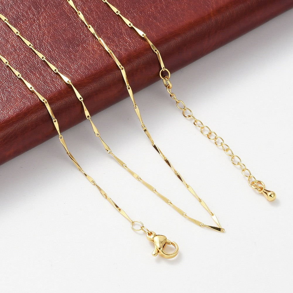 golden twisted bar link necklace with lobster claw clasp and extender chain draped over brown leather pad onto white surface.